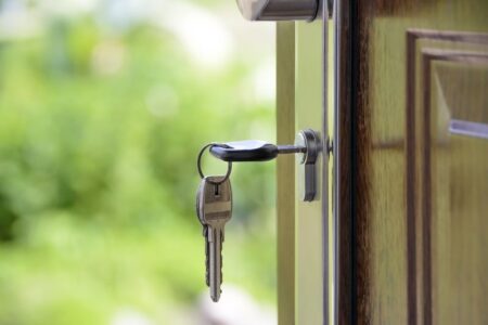 A key in a door lock, with the door slightly ajar and a blurry green background.