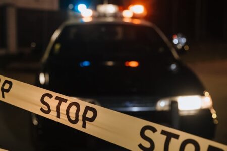 Police car with flashing lights behind yellow 'STOP' tape at night.