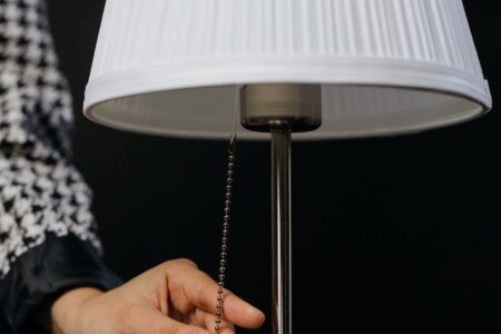 A hand pulls the chain on a table lamp with a white pleated shade, symbolizing a power outage.