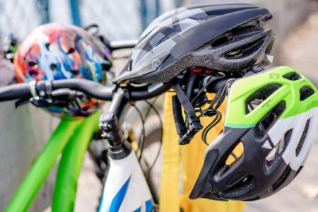 Multiple bicycle helmets in various colors hang on bike handlebars, representing cycling safety.
