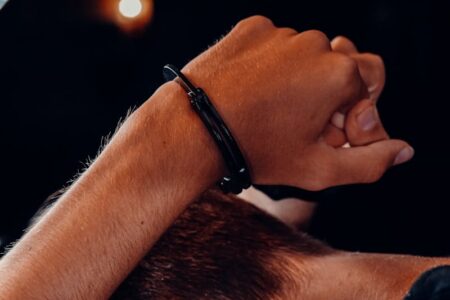 Close-up of a person's wrist with a black handcuff-like bracelet against a dark background.