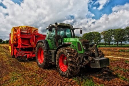 A green tractor with a red trailer in a muddy field under a cloudy sky.