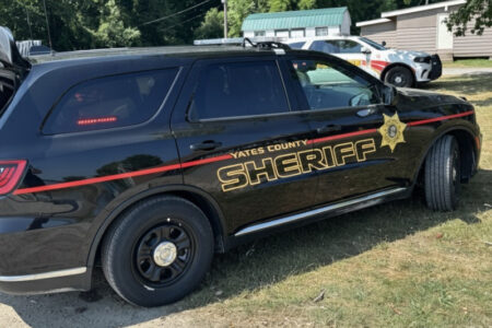Black Yates County Sheriff's SUV parked on grass with another police vehicle in the background.